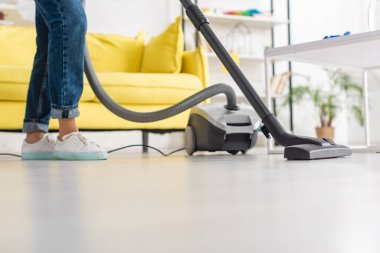 Oturma odasındaki kahve masasının yanında elektrikli süpürgeyle gezen kadın manzarası.