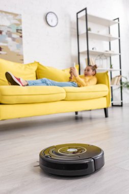 Çocuğun oturma odasındaki robotik elektrik süpürgesinin yanındaki kanepede yatmasının seçmeli odağı.