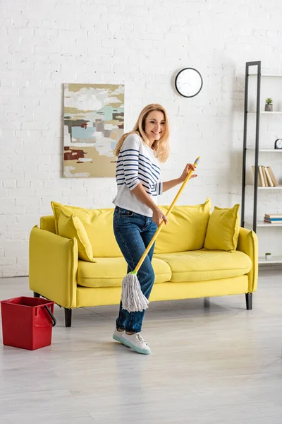 Hermosa Mujer Sosteniendo Fregona Cerca Cubo Sonriendo Sala Estar — Foto de Stock