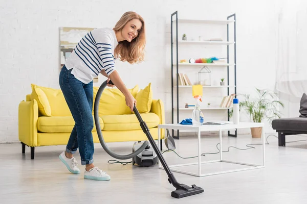 Mujer Sonriendo Limpiando Con Aspiradora Cerca Mesa Café Sofá Sala — Foto de Stock