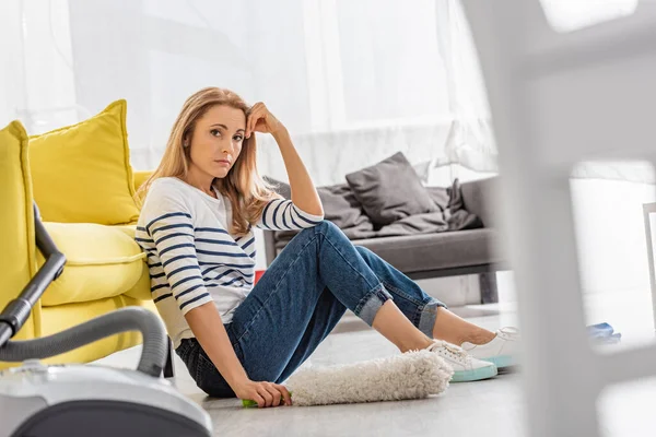 Selective Focus Tired Woman Feather Duster Looking Camera Sitting Sofa — Stock Photo, Image