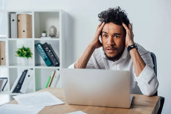 集中アフリカ系アメリカ人ビジネスマンの選択的フォーカスノートパソコンとオフィスのテーブルの上に紙の近くに座って — ストック写真