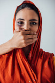 Männliche Hand bedeckt Mund zu indischer Frau mit blauen Flecken isoliert auf grau