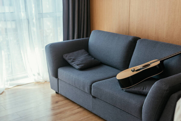 interior of living room with acoustic guitar on grey sofa and sunlight in large window