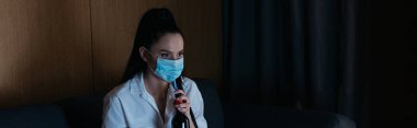 Medikal maskeli, elinde şarap şişesi olan depresif bir kadın.