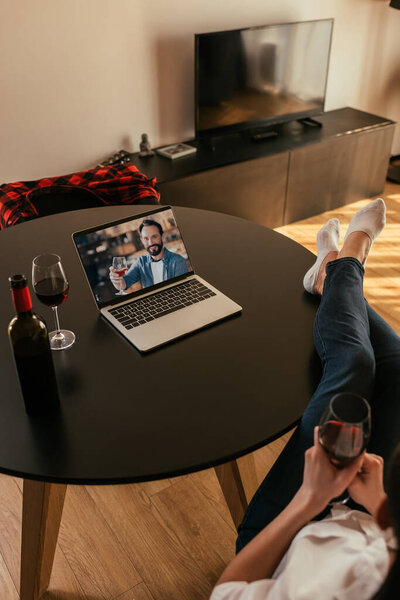 cropped view of woman and young man on screen of laptop holding glasses of red wine