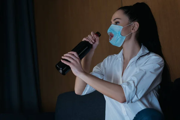 Καταθλιπτική Γυναίκα Ιατρική Μάσκα Τρύπα Κρατώντας Μπουκάλι Κρασί Ενώ Κάθεται — Φωτογραφία Αρχείου