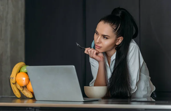 Mujer Reflexiva Sosteniendo Cuchara Cerca Del Ordenador Portátil Tazón Frutas — Foto de Stock