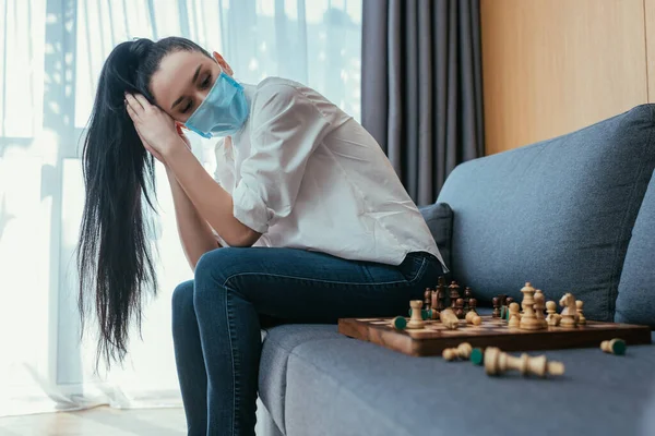 Sad Woman Protective Mask Looking Chessboard While Sitting Sofa — Stock Photo, Image