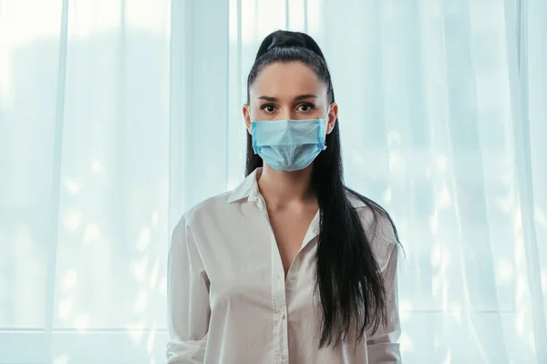Evdeki Pencerenin Yanında Duran Tıbbi Maskeli Ciddi Kız Kameraya Bakıyor — Stok fotoğraf