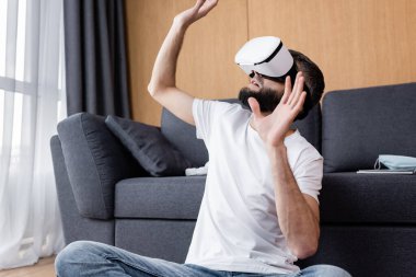 VR kulaklı bir adam oturma odasında yerde video oyunu oynuyor.