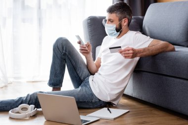 Medikal maskeli bir adam akıllı telefon ve kredi kartı kullanıyor. 