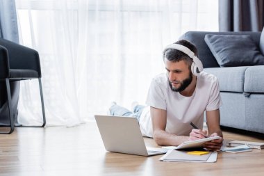 Kulaklıklı bir adam oturma odasında dizüstü bilgisayara bakıyor.