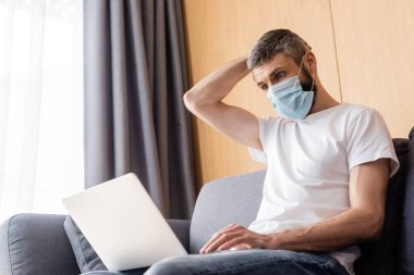 Maskeli serbest çalışan oturma odasında dizüstü bilgisayar kullanıyor.