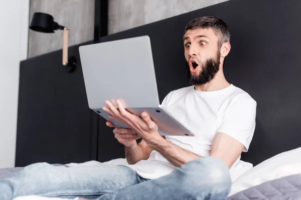 Επιλεκτική Εστίαση Του Σοκαρισμένος Άνθρωπος Κρατώντας Φορητό Υπολογιστή Στο Κρεβάτι — Φωτογραφία Αρχείου