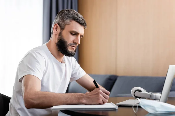 Foco Seletivo Teleworker Escrevendo Notebook Perto Laptop Máscara Médica Mesa — Fotografia de Stock