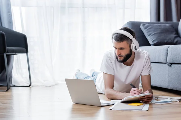 Man Hörlurar Skriver Anteckningsbok Och Tittar Bärbar Dator Webinar Vardagsrummet — Stockfoto