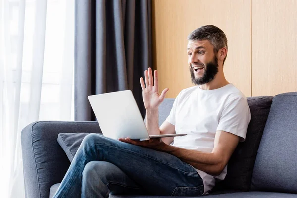 Side view of positive teleworker having video chat on laptop in living room