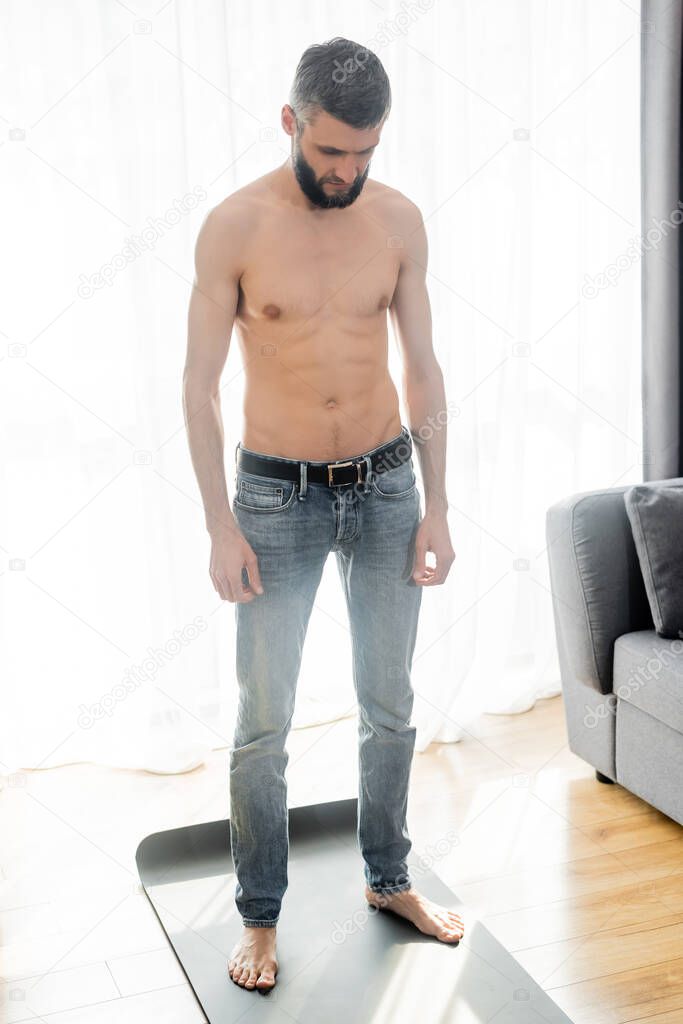 Shirtless man standing on fitness mat in living room