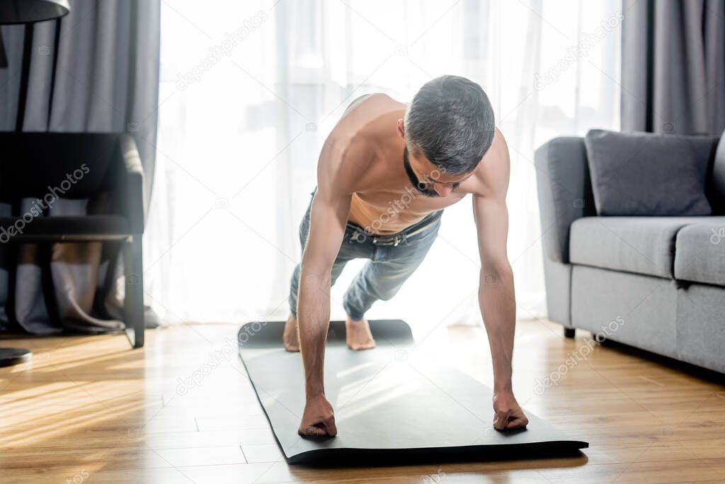 Shirtless man doing press ups while training on fitness mat in living room