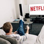 KYIV, UKRAINE - 14 Nisan 2020: Kotlu adam evde netflix ile televizyon ekranının yanında uzaktan kumanda tutuyor