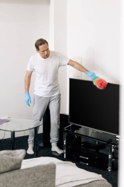 Oturma odasındaki boş TV ekranını temizlerken elinde fırça tutan adamın seçici odağı 