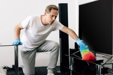 Oturma odasındaki boş TV ekranını temizlerken elinde fırça tutan adam. 