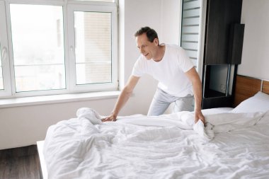 Modern yatak odasında beyaz battaniyeye dokunan mutlu bir adam. 