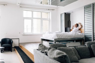 Modern yatak odasında esneyen mutlu bir adamın seçici odağı 