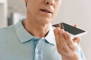 Akıllı telefonu boş ekran ile tutarken ses mesajı kaydeden adamın kırpılmış görüntüsü