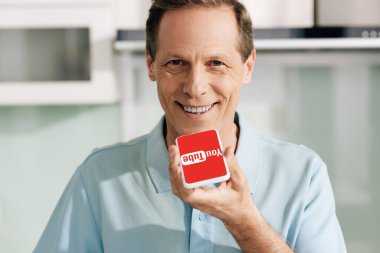 KYIV, UKRAINE - 14 Nisan 2020: Youtube uygulaması ile akıllı telefon tutan mutlu adam ekranda 