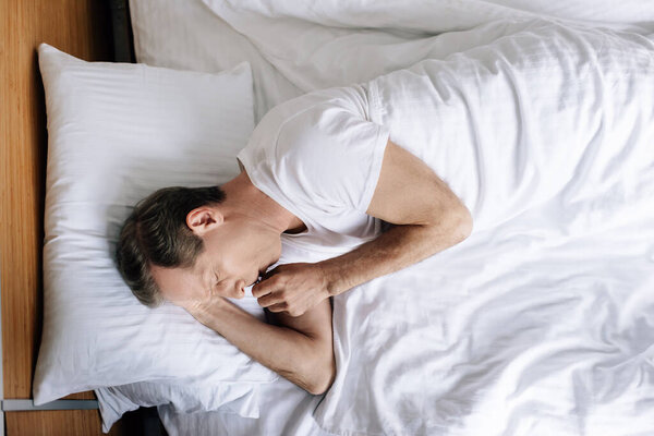 top view of sick man coughing while lying on bed 
