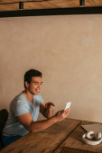 usmívající se smíšené rasy muž ukazuje a mají video hovor na smartphone doma na vlastní izolaci