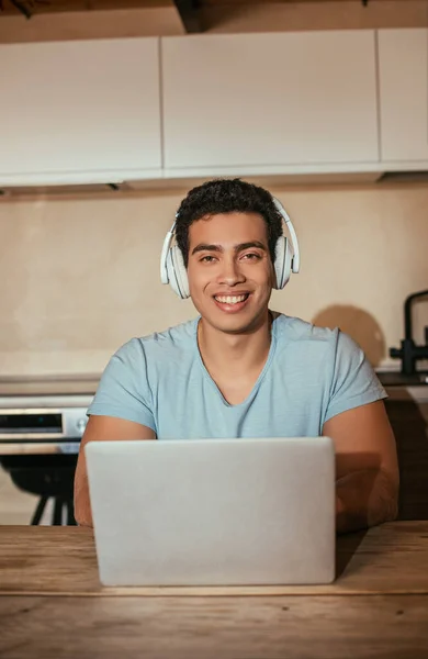 Sorrindo Racial Homem Ouvindo Música Com Fones Ouvido Usando Laptop — Fotografia de Stock