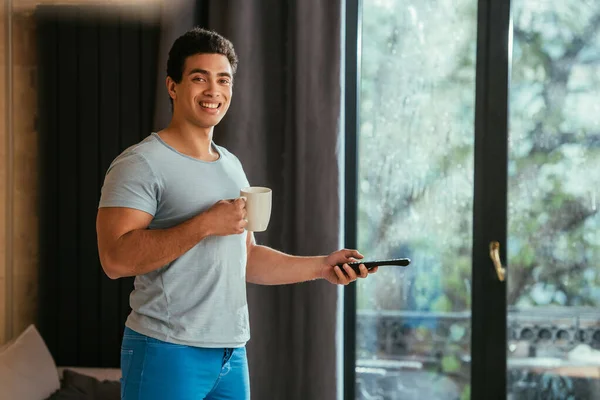 Smiling Mixed Race Man Holding Cup Coffee Remote Controller Home — Stock Photo, Image