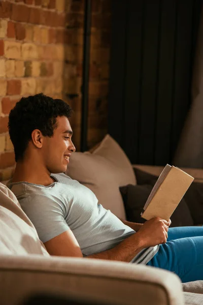 Bonito Sorrindo Misto Raça Homem Leitura Livro Sofá Durante Quarentena — Fotografia de Stock