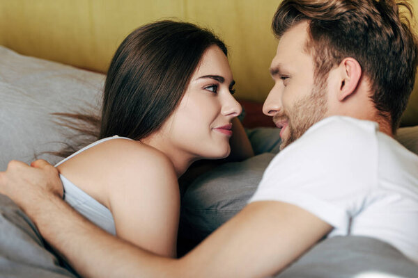 selective focus of happy man and cheerful woman looking at each other in bed 