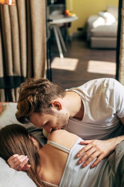 Yatakta sevgilisinin omzunu öpen sakallı adamın seçici odağı.