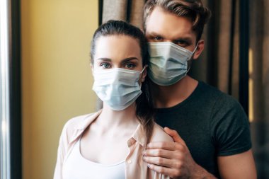 man hugging girlfriend in medical mask and looking at camera  clipart