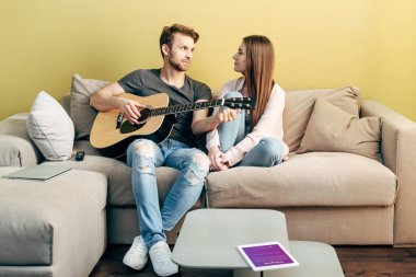 KYIV, UKRAINE - 22 Nisan 2020: Çekici bir kızın yanında akustik gitar çalan yakışıklı adam ve instagram uygulamalı dijital tablet 