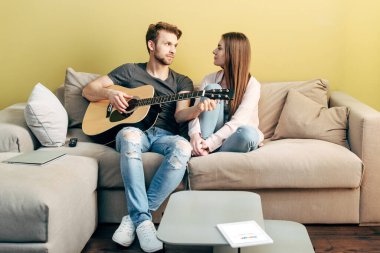 KYIV, UKRAINE - 22 Nisan 2020: yakışıklı adam çekici kızın yanında akustik gitar çalıyor ve Google uygulamalı dijital tablet 