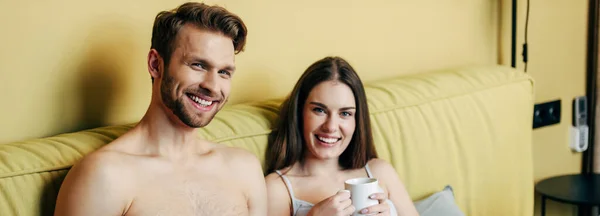 纵横交错的快乐的肌肉男人和快乐的女人一边举杯喝咖啡一边看着相机 — 图库照片