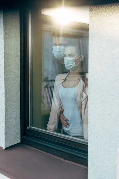 戴口罩的夫妇站在家里靠窗的位置 — 图库照片