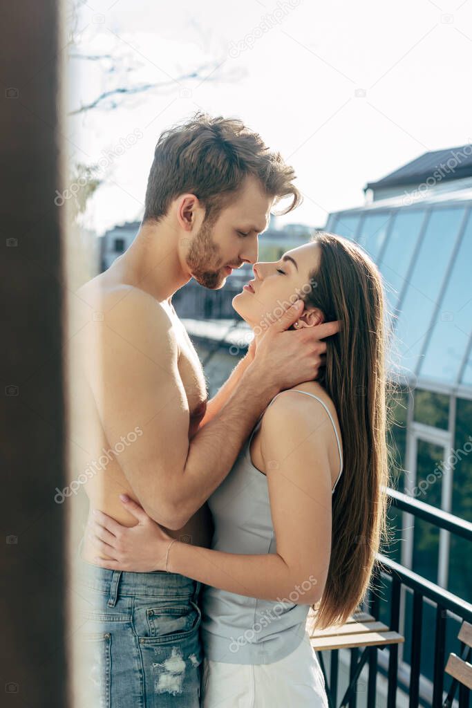 selective focus of shirtless man hugging girlfriend on balcony 