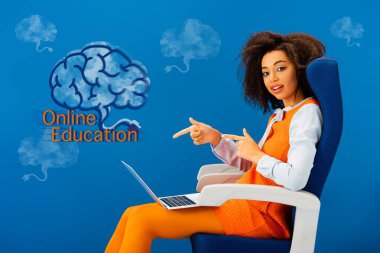 Afro-Amerikan kadın koltuğunda oturuyor ve parmaklarıyla mavi arkaplanda online eğitim illüstrasyonunu işaret ediyor.