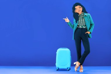 Mavi arka planda seyahat çantasının yanında duran resimli yüzü olan kadın parmağıyla işaret ediyor.