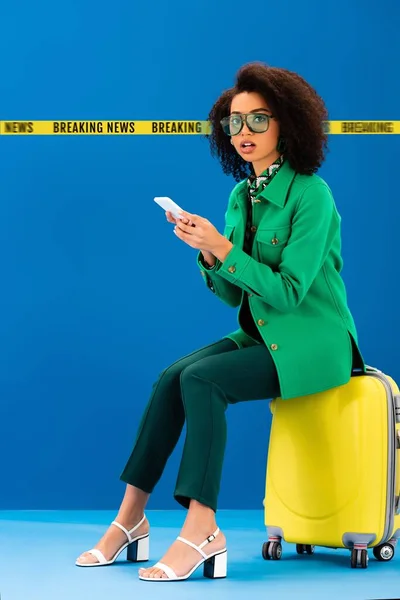 Chockad Afrikansk Amerikansk Kvinna Sitter Resväska Och Hålla Smartphone Blå — Stockfoto