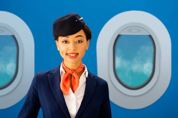smiling african american flight attendant looking at camera with portholes on blue background