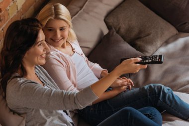 Oturma odasında uzaktan kumandayla annesine bakan gülümseyen çocuğun seçici odağı.