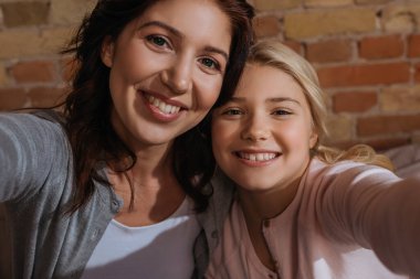 Happy mother and daughter smiling at camera at home  clipart